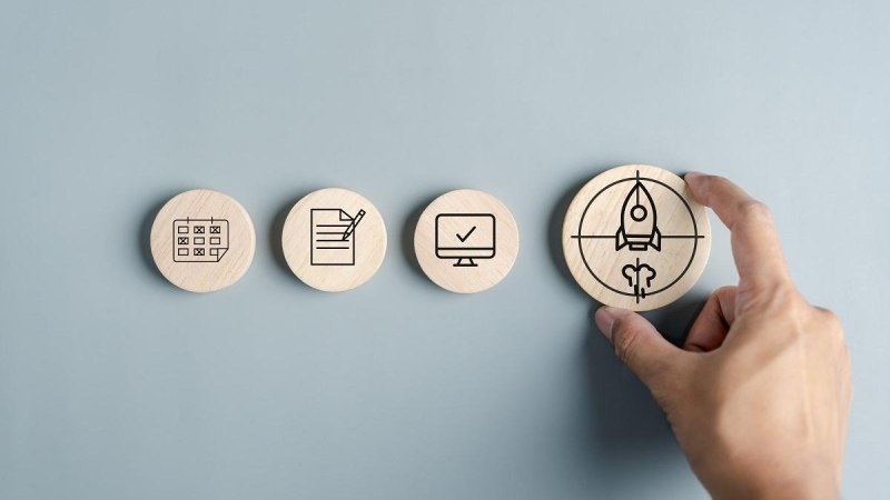 Vier Holzscheiben mit Symbolen: Kalender, Dokument, Computer mit Häkchen und Rakete. Eine Hand hält die Rakete. Grauer Hintergrund., © ©Kiattisak - stock.adobe.com