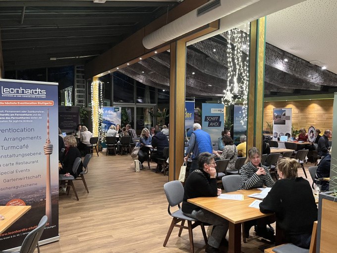 Gäste sitzen in einem stilvollen Restaurant mit großen Fenstern und Lichterketten. Ein Banner des Restaurants Leonhardts ist sichtbar., © SWR Media Services GmbH / SWR Fernsehturm Stuttgart
