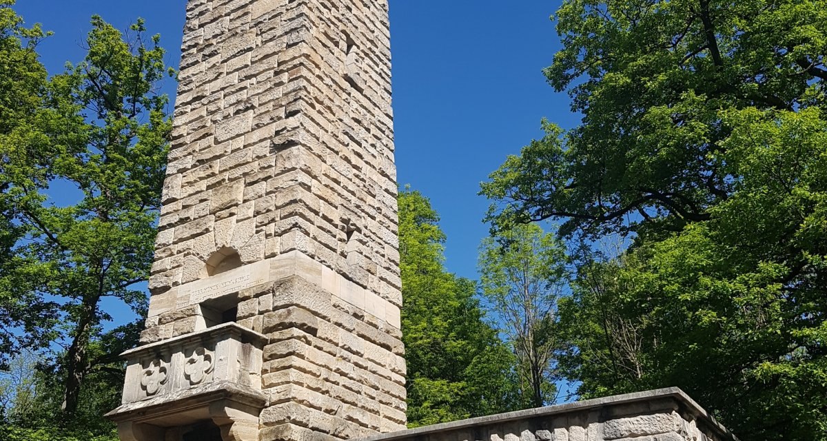 Der Kernenturm aus Stein erhebt sich vor einem klaren blauen Himmel, umgeben von grünen Bäumen. Im Vordergrund sind Stühle zu sehen., © Remstal Tourismus e.V. Der Kernenturm aus Stein erhebt sich vor einem klaren blauen Himmel, umgeben von grünen Bäumen. Im Vordergrund sind Stühle zu sehen., © Remstal Tourismus e.V.