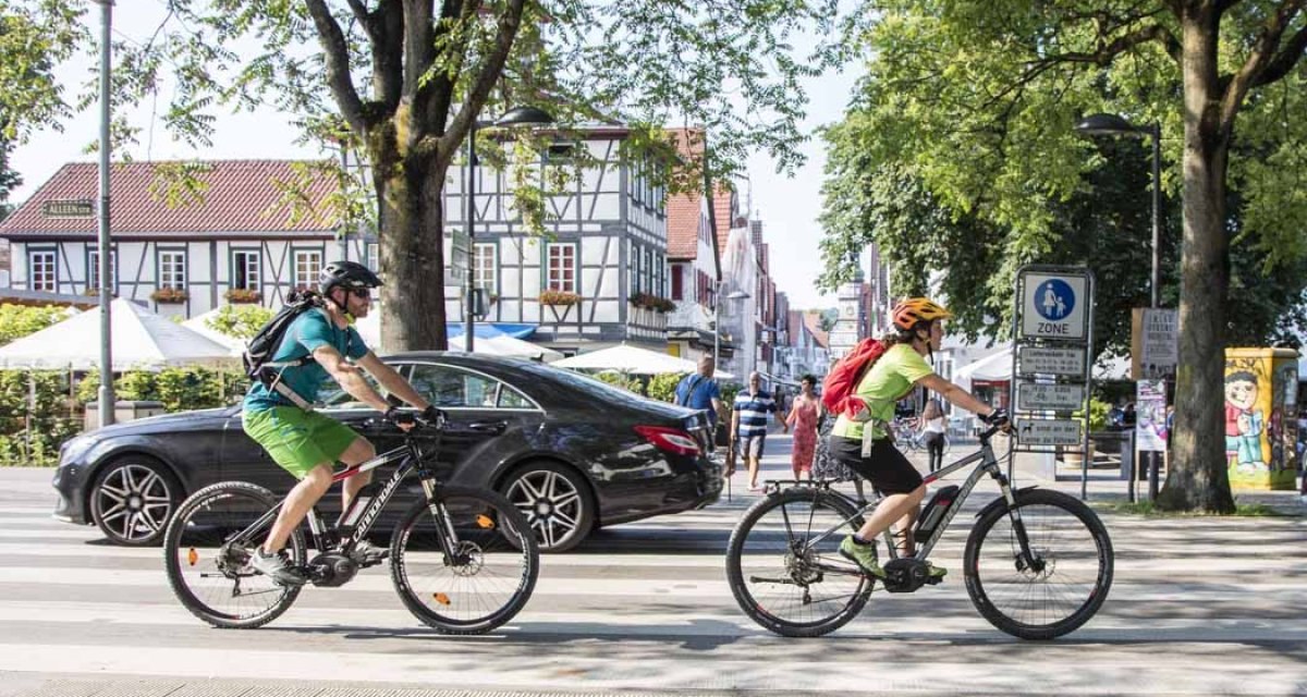Zwei Radfahrer überqueren einen Zebrastreifen in einer Stadt mit Fachwerkhäusern. Im Hintergrund sind Fußgänger und Bäume zu sehen., © Schwäbische Alb Tourismusverband e.V. Zwei Radfahrer überqueren einen Zebrastreifen in einer Stadt mit Fachwerkhäusern. Im Hintergrund sind Fußgänger und Bäume zu sehen., © Schwäbische Alb Tourismusverband e.V.