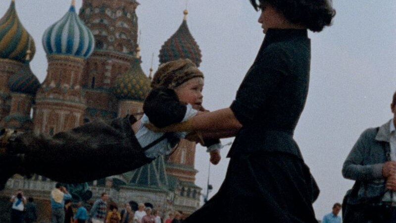Eine Frau schwingt ein Kind vor der Basilius-Kathedrale in Moskau. Im Hintergrund sind Menschen und die bunten Türme der Kathedrale zu sehen., © Kulturhaus Schwanen Eine Frau schwingt ein Kind vor der Basilius-Kathedrale in Moskau. Im Hintergrund sind Menschen und die bunten Türme der Kathedrale zu sehen., © Kulturhaus Schwanen