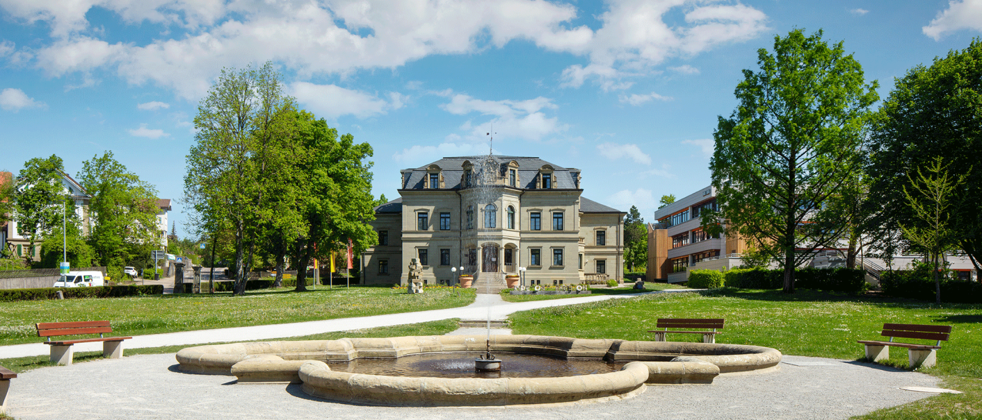 Das Neue Schloss in Gaildorf mit einem Brunnen im Vordergrund, umgeben von Bäumen und einem klaren blauen Himmel., © Stadt Gaildorf