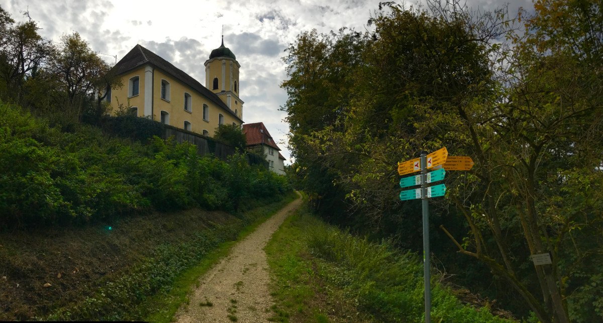 Ein Pfad führt zur Kirche in Türkheim, umgeben von Bäumen. Wegweiser stehen am Wegesrand, der Himmel ist bewölkt., © Landkreis Göppingen Ein Pfad führt zur Kirche in Türkheim, umgeben von Bäumen. Wegweiser stehen am Wegesrand, der Himmel ist bewölkt., © Landkreis Göppingen