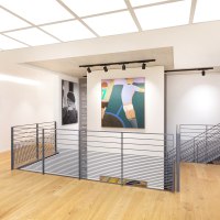 Moderne Galerie mit Holzboden, Gemälden an weißen Wänden und einem zentralen Treppengeländer. Helle Beleuchtung und minimalistisches Design., © Freundeskreis Fritz Genkinger e.V.
