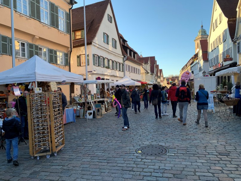 Menschen besuchen einen Kunsthandwerkermarkt in einer gepflasterten Straße mit Ständen und historischen Gebäuden., © Citymarketing Nürtingen_Werbeagentur Priss Menschen besuchen einen Kunsthandwerkermarkt in einer gepflasterten Straße mit Ständen und historischen Gebäuden., © Citymarketing Nürtingen_Werbeagentur Priss
