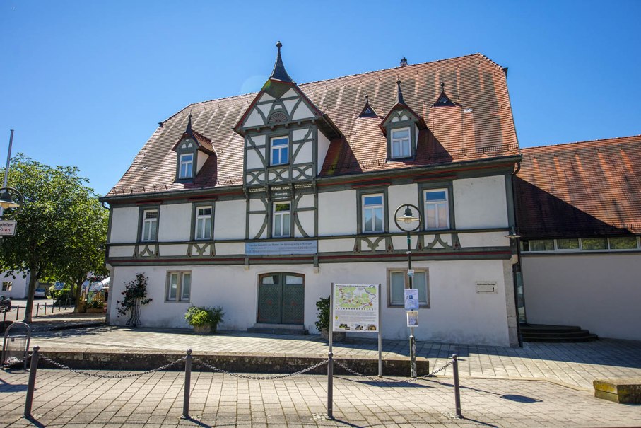 Fachwerkgebäude des Nürtinger Stadtmuseums mit rotem Dach und mehreren Fenstern, umgeben von Bäumen und einem gepflasterten Vorplatz., © SMG, Achim Mende