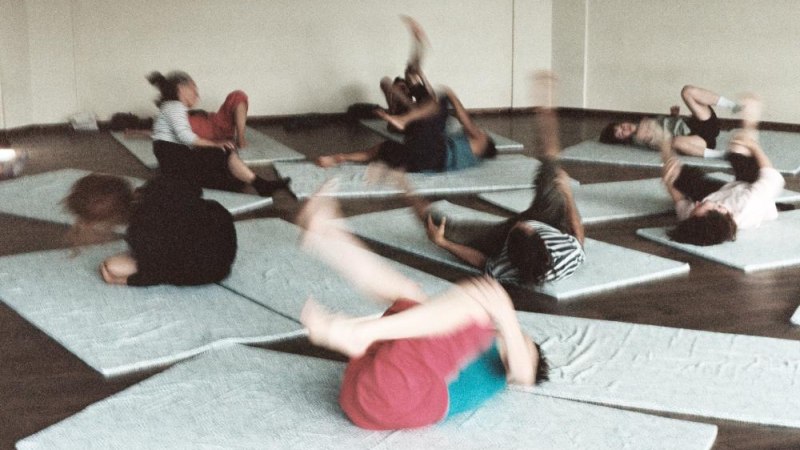 Menschen liegen auf Matten in einem Raum und führen dynamische Bewegungsübungen durch. Die Szene wirkt lebendig und energetisch., © © Geoffrey Delahaye Menschen liegen auf Matten in einem Raum und führen dynamische Bewegungsübungen durch. Die Szene wirkt lebendig und energetisch., © © Geoffrey Delahaye