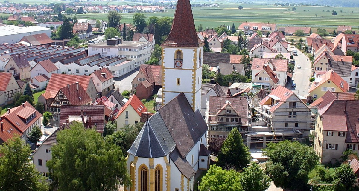 Luftaufnahme von Holzgerlingen mit einer Kirche im Vordergrund, umgeben von Häusern und grüner Landschaft im Hintergrund., © Natur.Nah. Schönbuch & Heckengäu Luftaufnahme von Holzgerlingen mit einer Kirche im Vordergrund, umgeben von Häusern und grüner Landschaft im Hintergrund., © Natur.Nah. Schönbuch & Heckengäu
