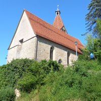Kirche oberhalb eines Hanges von unten aufgenommen. Helles Steingebäude mit rotem Ziegeldach und, vom Gebäude fast verdeckten, Kirchturm. Die Kirche ist umgeben von üppigem Grün, mit einem klaren blauen Himmel im Hintergrund., © Petra Natzkowski Kirche oberhalb eines Hanges von unten aufgenommen. Helles Steingebäude mit rotem Ziegeldach und, vom Gebäude fast verdeckten, Kirchturm. Die Kirche ist umgeben von üppigem Grün, mit einem klaren blauen Himmel im Hintergrund., © Petra Natzkowski