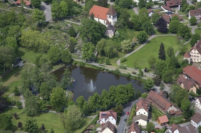 Luftaufnahme von Murrhardt: Kirche, Teich mit Springbrunnen, umgeben von gr&uuml;nen B&auml;umen und Geb&auml;uden., &copy; Stadt Murrhardt