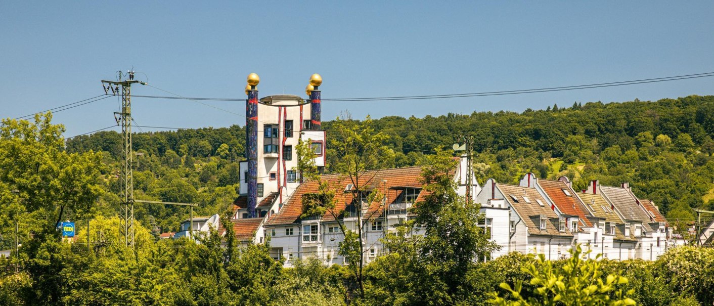 Das Hundertwasserhaus in Plochingen mit seinen bunten S&auml;ulen und goldenen Kugeln, umgeben von gr&uuml;ner Landschaft und B&auml;umen., &copy; Stuttgart-Marketing GmbH, Sarah Schmid
