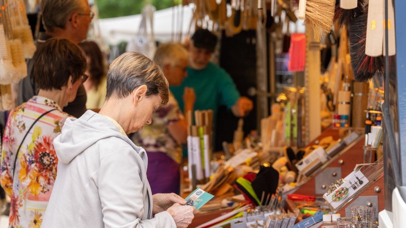 Menschen st&ouml;bern an einem Marktstand voller B&uuml;rsten und Haushaltswaren auf einem Sommermarkt in N&uuml;rtingen., &copy; J&uuml;rgen Hackenjos