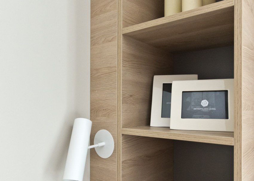 Ein Holzregal mit Kerzen, Bilderrahmen und einer weißen Wandlampe. Die Deko ist minimalistisch und modern., © Arthotel Ana / elaya