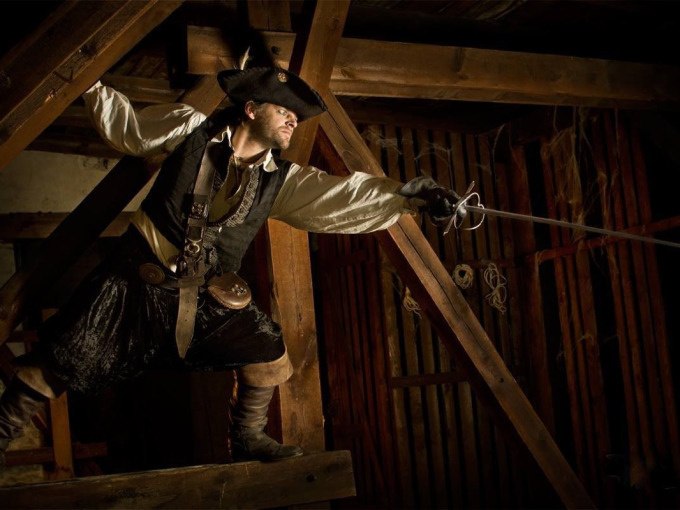 Person in Piratenkostüm posiert mit Degen in einem hölzernen Raum, dramatische Beleuchtung., © Esslinger Stadtmarketing &amp; Tourismus GmbH