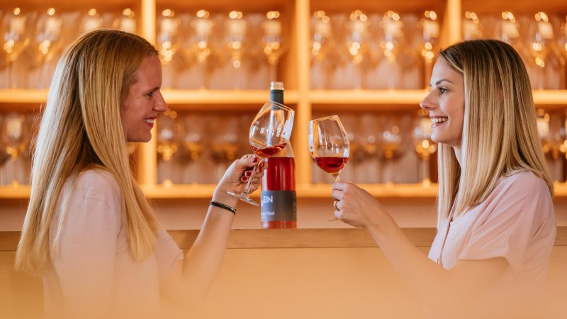 Zwei Frauen sto&szlig;en mit Weingl&auml;sern in einer Vinothek an. Im Hintergrund sind Weinflaschen und Gl&auml;ser zu sehen., &copy; Stuttgart-Marketing GmbH, Thomas Niederm&uuml;ller