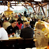 Ein belebtes Brauhaus mit vielen Menschen, die an Tischen sitzen. Im Hintergrund sind große Kupferkessel zu sehen., © Stuttgart-Marketing GmbH