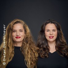 Zwei Frauen mit langen Haaren und roten Lippen posieren vor einem dunklen Hintergrund., &copy; links im Bild