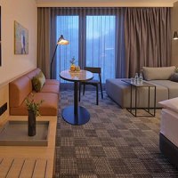 Modernes Hotelzimmer mit Sofa, Tisch, Bett und großen Fenstern. Dezente Beleuchtung und stilvolle Dekoration schaffen eine gemütliche Atmosphäre., © Adina Apartment Hotel Stuttgart