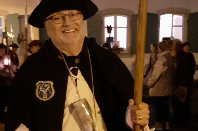 Ein Mann in Nachtwächterkleidung mit Hut und Stab lächelt in die Kamera. Im Hintergrund sind Menschen und ein beleuchtetes Gebäude zu sehen., © WTM GmbH Waiblingen Ein Mann in Nachtwächterkleidung mit Hut und Stab lächelt in die Kamera. Im Hintergrund sind Menschen und ein beleuchtetes Gebäude zu sehen., © WTM GmbH Waiblingen