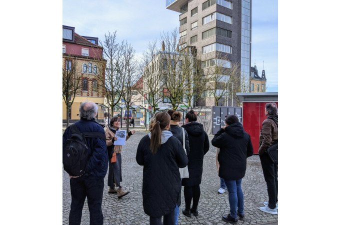 Eine Gruppe von Menschen betrachtet ein modernes Hochhaus auf einem gepflasterten Platz. Im Hintergrund sind weitere Gebäude und Bäume zu sehen., © Eigenbetrieb Tourismus und Citymanagement Schorndorf Eine Gruppe von Menschen betrachtet ein modernes Hochhaus auf einem gepflasterten Platz. Im Hintergrund sind weitere Gebäude und Bäume zu sehen., © Eigenbetrieb Tourismus und Citymanagement Schorndorf