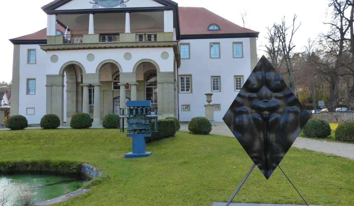 Schloss D&auml;tzingen mit modernen Skulpturen im Vordergrund, umgeben von gepflegtem Rasen und einem kleinen Teich., &copy; Natur.Nah. Sch&ouml;nbuch & Heckeng&auml;u