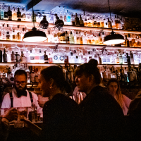 Eine stimmungsvolle Bar mit beleuchteten Flaschenregalen. Menschen unterhalten sich, w&auml;hrend ein Barkeeper Getr&auml;nke zubereitet., &copy; Stuttgart-Marketing GmbH, Sarah Schmid