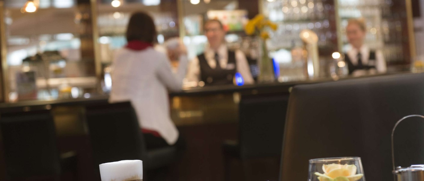 Ein Tisch in einem Café mit Kaffee, Wasser und Gebäck. Im Hintergrund eine Theke mit Bedienung und der Schriftzug 'Café Espresso'., © Maritim Hotelgesellschaft mbH