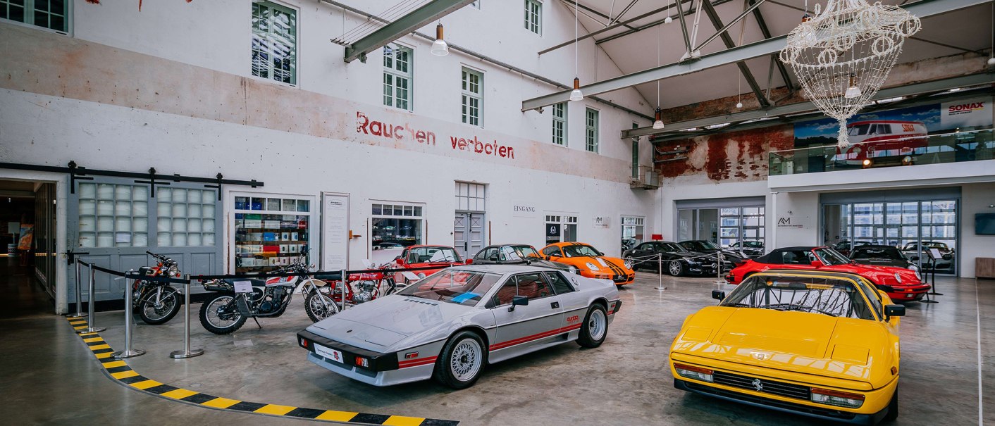 Innenansicht der Motorworld Region Stuttgart mit klassischen Autos und Motorrädern in einer Halle mit hohen Decken und einem Kronleuchter., © Stuttgart-Marketing GmbH, Thomas Niedermüller