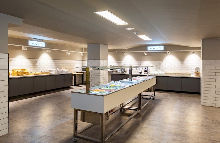 Ein modernes Frühstücksbuffet in einem hellen Raum mit Fliesenwänden und mehreren Essensstationen., © A&O Hostels Marketing GmbH Ein modernes Frühstücksbuffet in einem hellen Raum mit Fliesenwänden und mehreren Essensstationen., © A&O Hostels Marketing GmbH