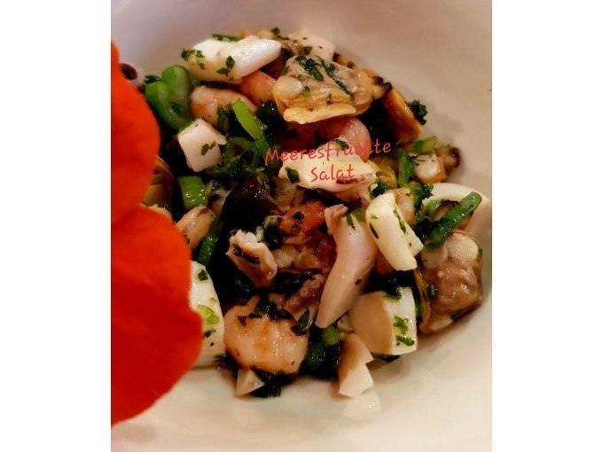 Meeresfrüchtesalat mit Kräutern und Gemüse in einer Schüssel, dekoriert mit einer orangefarbenen Blume., © Kultweine-Kochwelten-Kunstücke - Kochschule Sonja Lenz Meeresfrüchtesalat mit Kräutern und Gemüse in einer Schüssel, dekoriert mit einer orangefarbenen Blume., © Kultweine-Kochwelten-Kunstücke - Kochschule Sonja Lenz