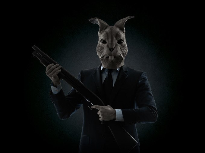 Eine Person im Anzug mit einem Hasenkopf hält ein Gewehr in einer dunklen Umgebung., © ExitGames Stuttgart Eine Person im Anzug mit einem Hasenkopf hält ein Gewehr in einer dunklen Umgebung., © ExitGames Stuttgart