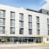 Modernes Hotelgebäude mit Glasfassade, Beschilderung 'Hotel' und 'Rezeption', umgeben von Grünflächen., © B&B Hotel Stuttgart-Neckarhafen