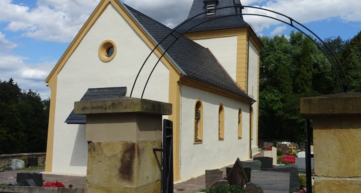 Die Ottilienkirche Bettringen mit gelben Akzenten, umgeben von einem Friedhof, unter einem blauen Himmel mit weißen Wolken., © Foto: Cornelia Steinbach Die Ottilienkirche Bettringen mit gelben Akzenten, umgeben von einem Friedhof, unter einem blauen Himmel mit weißen Wolken., © Foto: Cornelia Steinbach