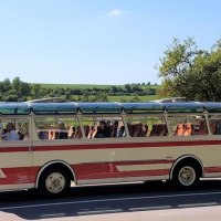 Ein Oldtimerbus mit Glasdach f&auml;hrt durch eine l&auml;ndliche Landschaft der Schw&auml;bischen Alb. Der Himmel ist klar und blau., &copy; SwabianTravel