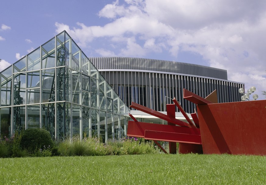 Glasgebäude und rote Skulptur im Stadthallenpark Sindelfingen, umgeben von grüner Wiese und blauem Himmel., © Stadt Sindelfingen Glasgebäude und rote Skulptur im Stadthallenpark Sindelfingen, umgeben von grüner Wiese und blauem Himmel., © Stadt Sindelfingen