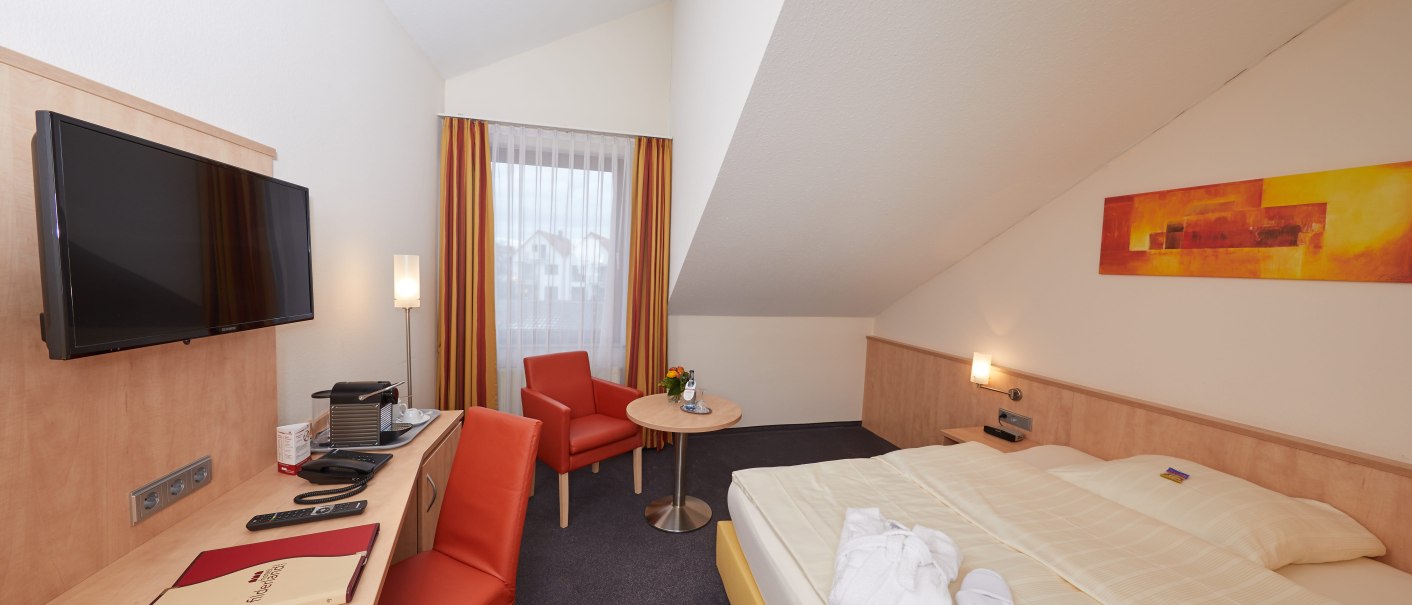 Ein gemütliches Einzelzimmer mit Bett, Schreibtisch, Fernseher und Sitzbereich. Helle Farben und moderne Einrichtung dominieren den Raum., © TOMAS