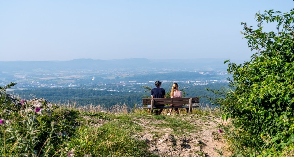 Zwei Personen sitzen auf einer Bank und genießen die Aussicht auf eine weite Landschaft unter klarem Himmel., © TMBW, Gregor Lengler Zwei Personen sitzen auf einer Bank und genießen die Aussicht auf eine weite Landschaft unter klarem Himmel., © TMBW, Gregor Lengler