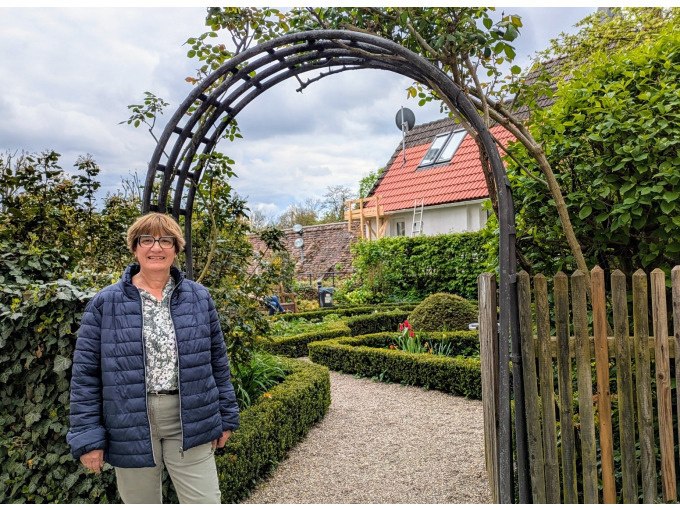 Frau vor einem Gartenbogen, umgeben von gepflegtem Garten mit Hecken und Blumen. Im Hintergrund ein Haus mit rotem Dach., &copy; WTM GmbH Waiblingen
