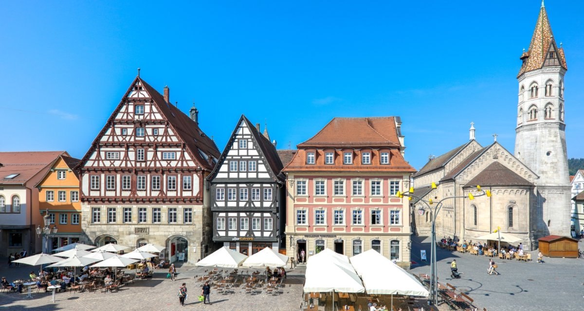 Historische Fachwerkh&auml;user und eine Kirche am Marktplatz von Schw&auml;bisch Gm&uuml;nd bei sonnigem Wetter. Menschen sitzen unter Sonnenschirmen., &copy; T&M GmbH Schw&auml;bisch Gm&uuml;nd