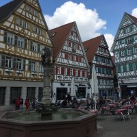Fachwerkhäuser am Marktplatz in Herrenberg, Deutschland. Ein Brunnen steht im Vordergrund, umgeben von Menschen und Cafétischen. Der Himmel ist blau mit Wolken., © www.pro-cycl.de