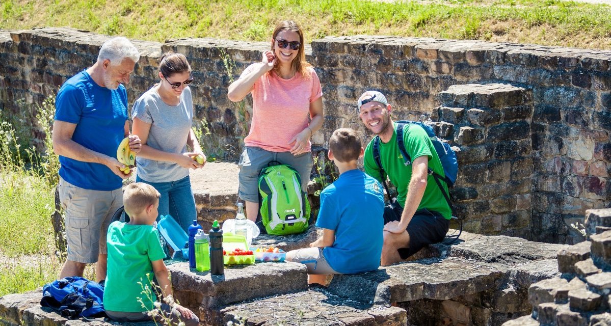 Eine Gruppe von Menschen macht ein Picknick auf alten Steinmauern im Freien. Sie haben Rucksäcke und Essen dabei., © hochgehberge Eine Gruppe von Menschen macht ein Picknick auf alten Steinmauern im Freien. Sie haben Rucksäcke und Essen dabei., © hochgehberge