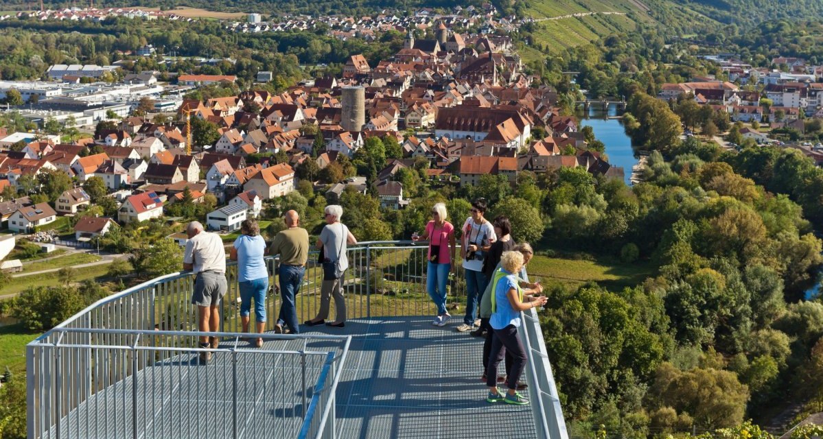 Menschen stehen auf einer Aussichtsplattform und blicken auf die Stadt Besigheim mit ihren roten Dächern und die umliegende grüne Landschaft., © Boris Lehner Menschen stehen auf einer Aussichtsplattform und blicken auf die Stadt Besigheim mit ihren roten Dächern und die umliegende grüne Landschaft., © Boris Lehner