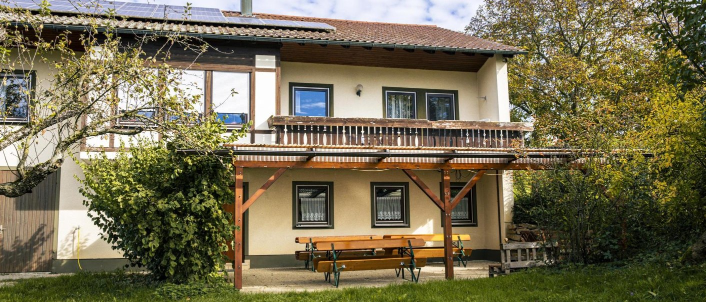 Zweistöckiges Gebäude mit Balkon, Solarpanelen auf dem Dach, umgeben von Bäumen. Eine Holzbank steht davor., © Stuttgart Marketing GmbH, Sarah Schmid