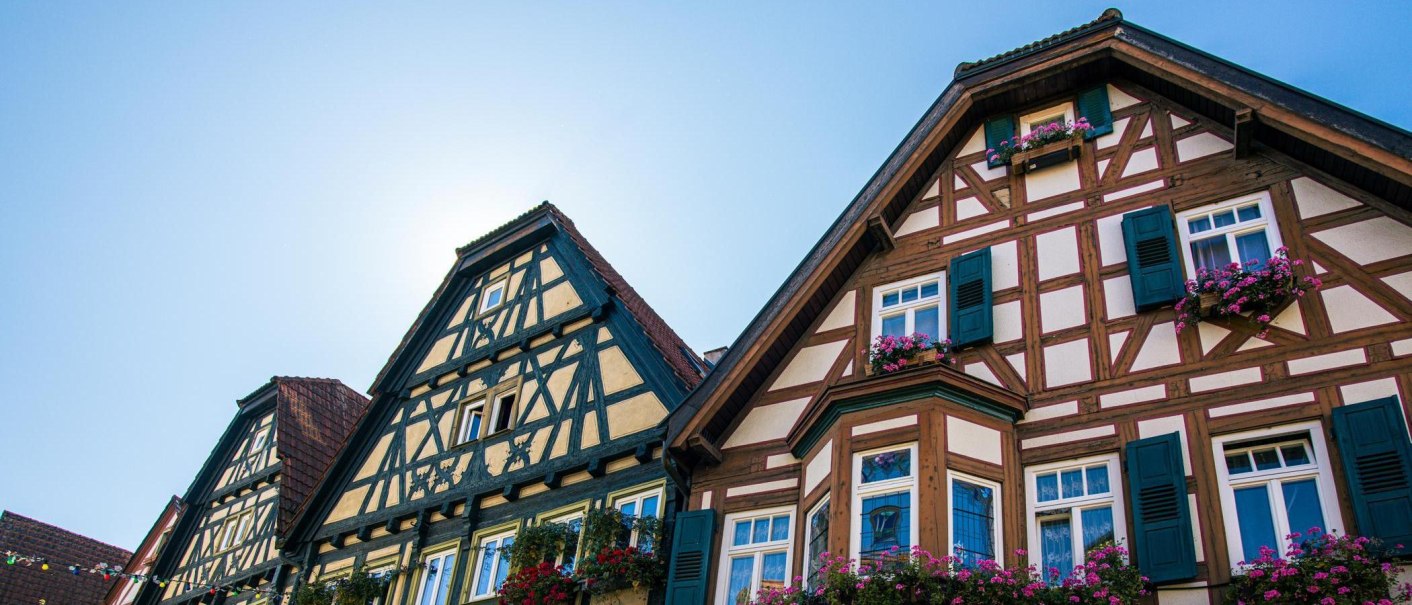Fachwerkhäuser in Besigheim mit blühenden Fensterkästen vor klarem, blauem Himmel. Traditionelle Architektur mit farbenfrohen Details., © Stuttgart-Marketing GmbH, Sarah Schmid