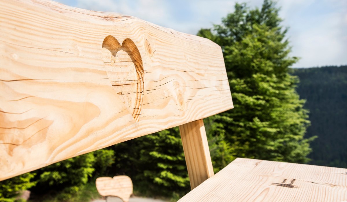 Nahaufnahme einer Holzbank mit Herzschnitzerei, im Hintergrund Bäume und blauer Himmel., © Nördlicher Schwarzwald Nahaufnahme einer Holzbank mit Herzschnitzerei, im Hintergrund Bäume und blauer Himmel., © Nördlicher Schwarzwald