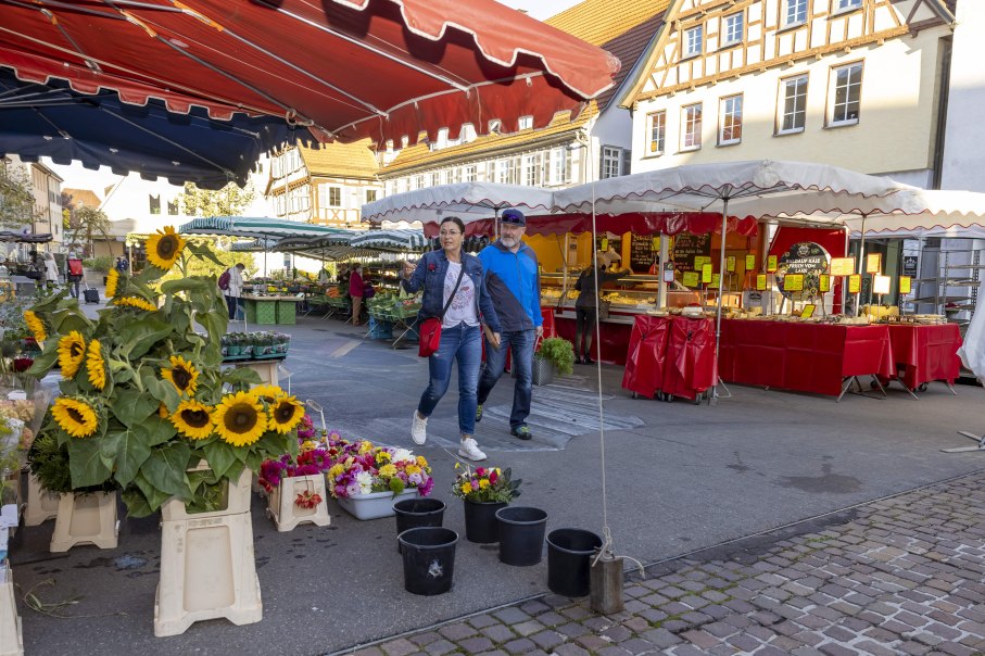 Ein Paar spaziert &uuml;ber einen Markt in Kirchheim unter Teck. Im Vordergrund stehen Sonnenblumen, im Hintergrund sind Marktst&auml;nde mit roten Planen., &copy; Torsten Wenzler