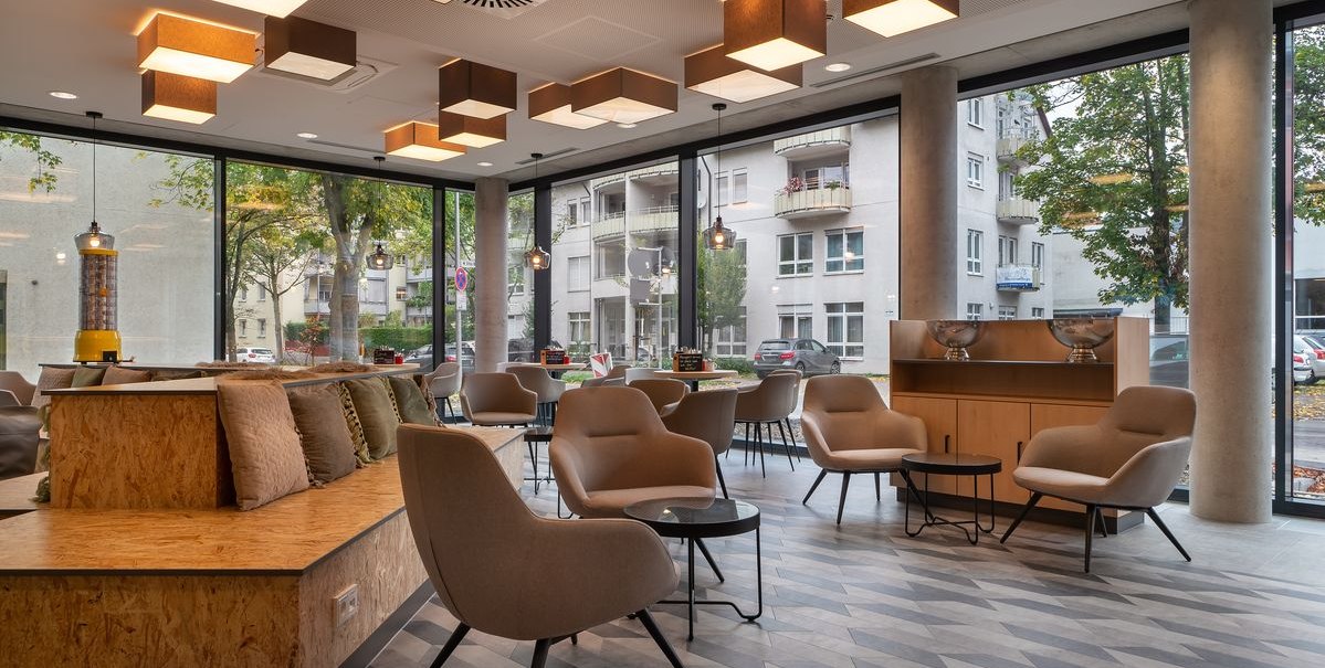 Moderne Lobby mit bequemen Sesseln, Tischen und großen Fenstern. Geometrische Deckenleuchten und ein Blick auf die Straße im Hintergrund., © Novum Hospitality Moderne Lobby mit bequemen Sesseln, Tischen und großen Fenstern. Geometrische Deckenleuchten und ein Blick auf die Straße im Hintergrund., © Novum Hospitality