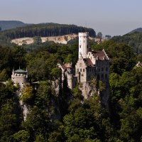 Schloss Lichtenstein thront majestätisch auf einem bewaldeten Hügel, umgeben von dichtem Wald und sanften Hügeln im Hintergrund., © Stuttgart-Marketing GmbH