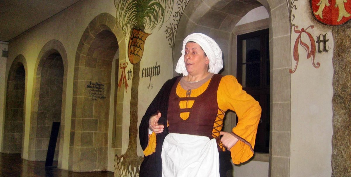 Frau in historischem Kostüm führt durch das Residenzschloss Bad Urach. Sie trägt ein gelbes Kleid mit braunem Mieder und eine weiße Haube.
