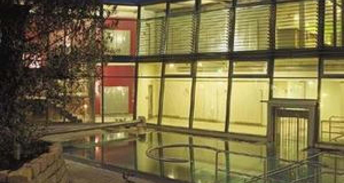 Modernes Gebäude mit Glasfassade, beleuchtet bei Nacht. Ein kleiner Pool oder Wasserfläche spiegelt das Licht wider. Bäume im Vordergrund., © Schwäbische Alb Modernes Gebäude mit Glasfassade, beleuchtet bei Nacht. Ein kleiner Pool oder Wasserfläche spiegelt das Licht wider. Bäume im Vordergrund., © Schwäbische Alb